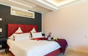 A modern bedroom with a red upholstered headboard, a large mirror, and a bedside table with a lamp. - Beach front apartment in Binz with indoor swimming pool (Prora/Rügen)