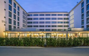 Un hotel moderno con fachada plana, varios pisos y una entrada bien iluminada.