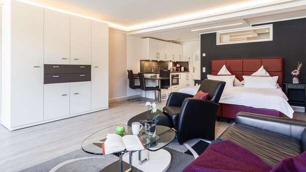 Ein modernes Hotelzimmer mit Bett, Sitzgelegenheit und Küchenzeile.