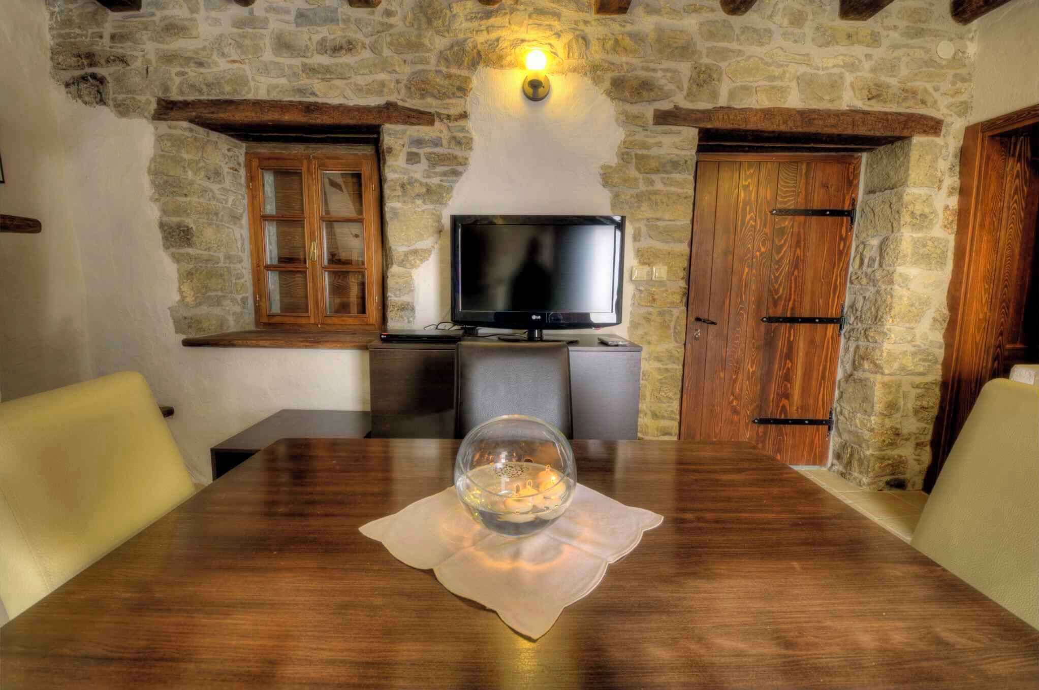 A rustic dining area with a wooden table, a glass bowl centerpiece, and stone walls.