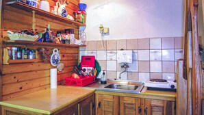 Een keuken met houten kastjes, een spoelbak en diverse keukenbenodigdheden op planken.
