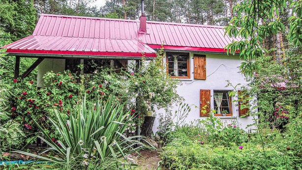 Een huis met een rood dak, omringd door weelderige begroeiing en bloeiende planten.