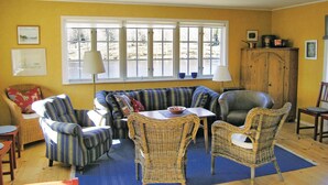A cozy living room with a blue-striped sofa, wicker chairs, a wooden cabinet, and a large window with a view of a snowy landscape. - 4 bedroom nice home in Bottnaryd (Bottnaryd)