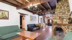 A spacious living area with a stone fireplace, wooden ceiling beams, and a green sofa. - Beautiful home in Sayalonga (Sayalonga)