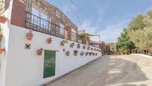 A narrow street with a white building featuring a green door, multiple potted plants, and a stone facade. - Beautiful home in Sayalonga (Sayalonga)