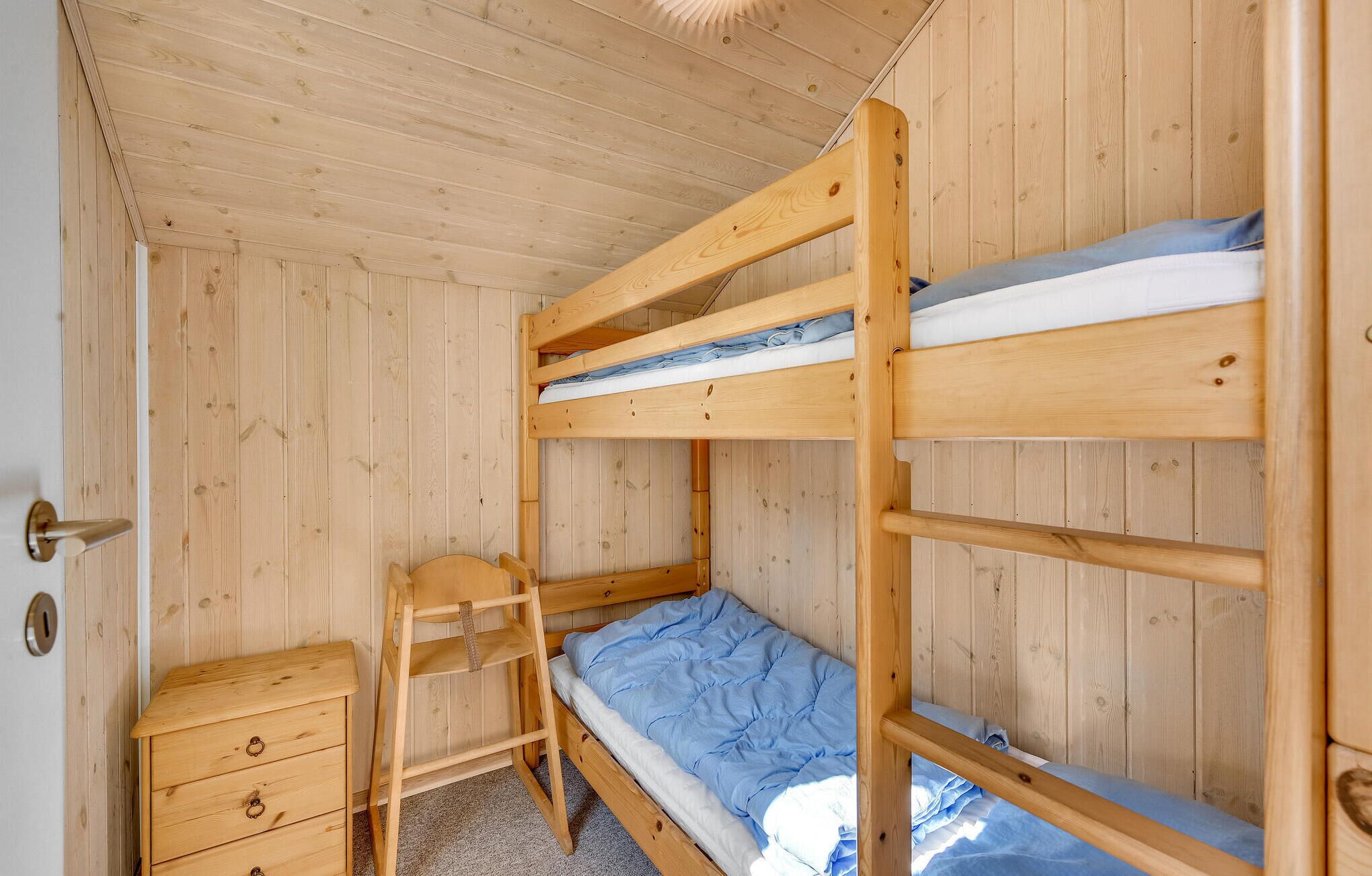 Una camera con un letto a castello, una scala in legno e un piccolo comò di legno.