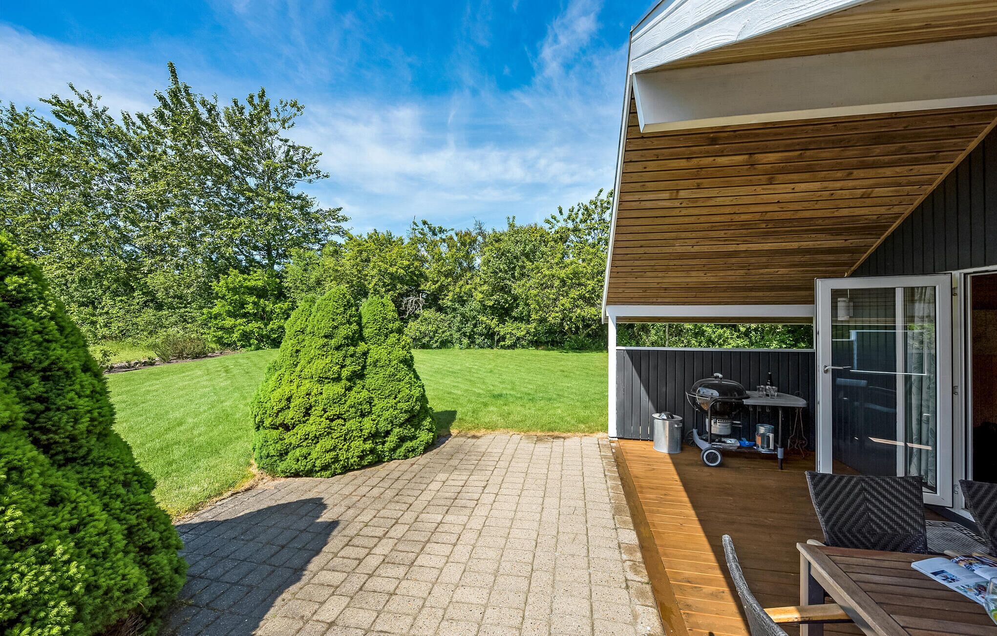 A patio area with a grill, seating, and a view of a well-maintained lawn and trees.
