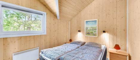 A wooden-paneled bedroom with a bed, a window, a radiator, and a poster on the wall.