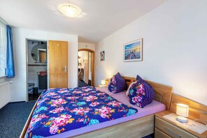 Ein Schlafzimmer mit floralem Bettbezug, einem hölzernen Kopfende, einem Nachttisch mit Lampe und einem Bild an der Wand.