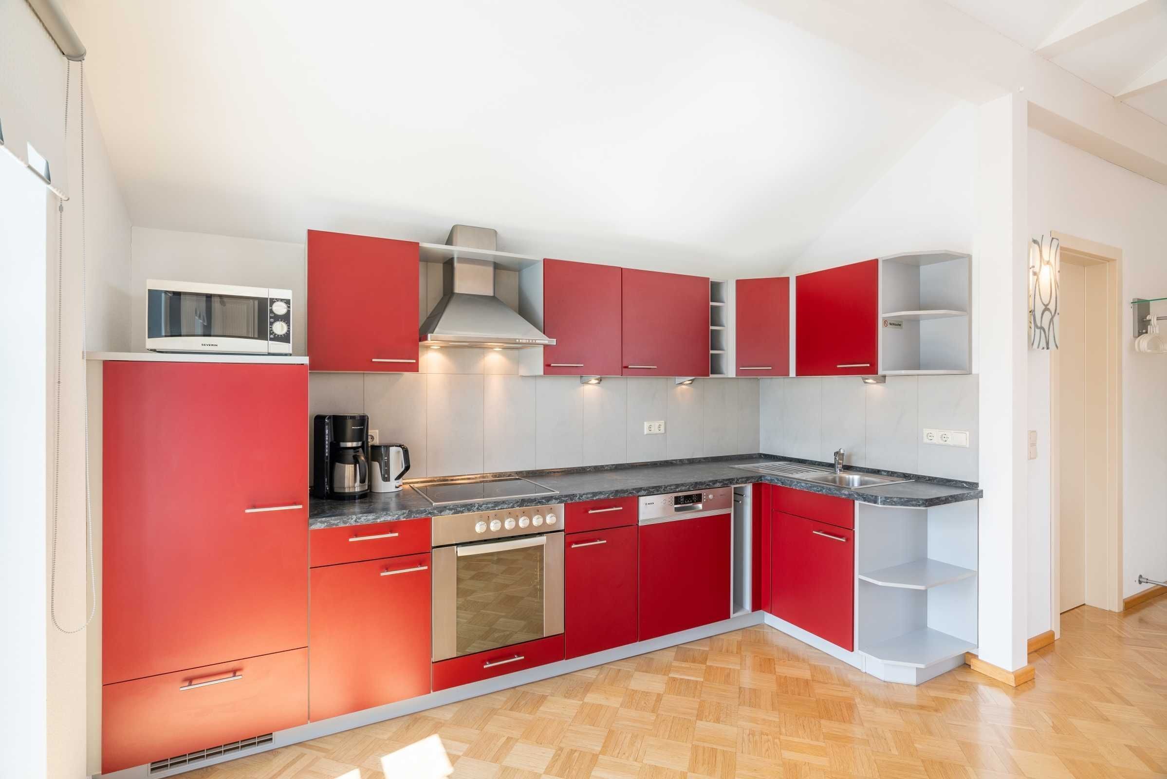 A compact kitchen with red cabinets, a microwave, a coffee maker, and a dishwasher.