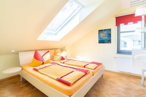 Une chambre avec un puits de lumière, un lit avec une couette orange, une table de chevet et un radiateur.