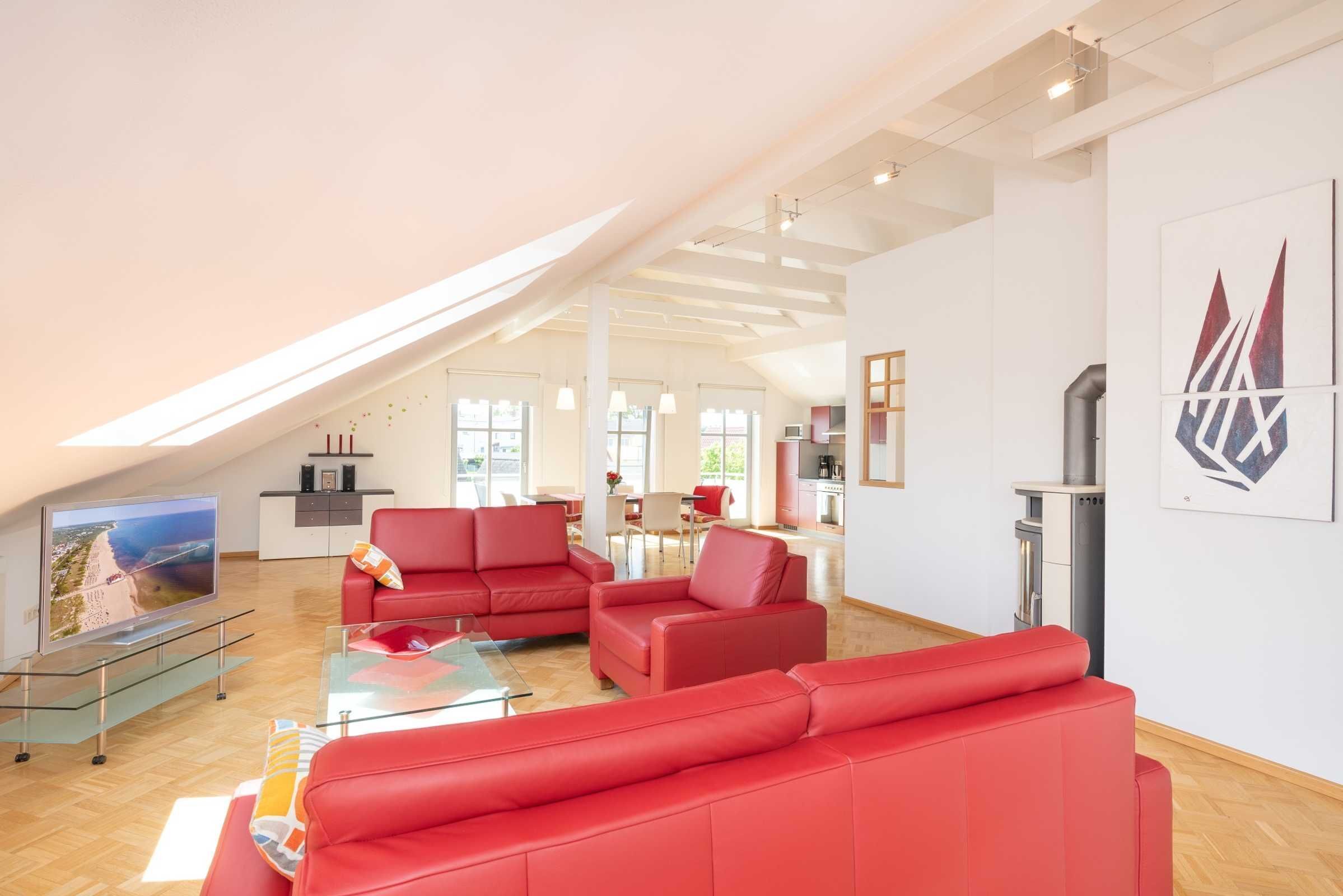 A spacious living area with a red sofa set, a glass coffee table, and a flat-screen TV.