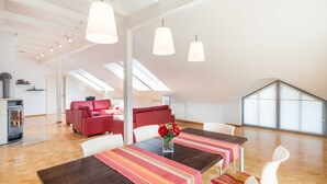Amplia sala de estar con techo alto, una mesa de comedor con mantel a rayas, un sofá rojo y una chimenea.
