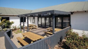 A covered patio with wooden tables and benches, a white building with large windows, and a clear sky. - Awesome home in Thyborøn with sauna (Thyborøn)