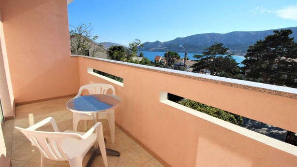 Un balcon avec une table et des chaises, donnant sur un plan d’eau et des montagnes.