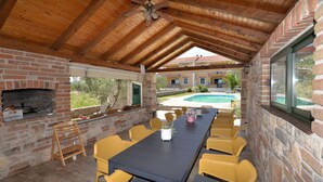 Un patio al aire libre con chimenea de ladrillo, sillas de mimbre amarillo, una mesa larga y vista a una piscina.