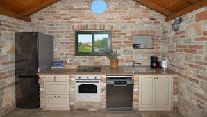 Una cocina con pared de ladrillo, ventana, refrigerador, horno, lavavajillas y pileta.