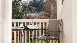 Un espacio al aire libre cubierto con una mesa, una silla, piso de madera y vistas a árboles y edificios.