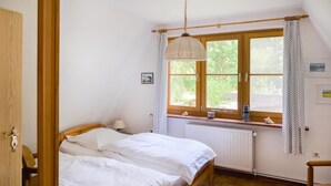 A bedroom with a wooden bed, a window with curtains, a radiator, and a small table with a lamp. - Gorgeous apartment in Prerow with WiFi (Prerow)