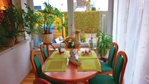 A dining area with a round table, green upholstered chairs, and potted plants.