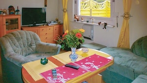 A living room with a television, a sofa, a chair, a table with a vase of flowers, and a window with curtains.