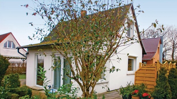 A white house with a sloped roof, a wooden fence, and a garden with potted plants.