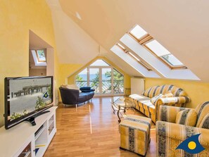 Ein geräumiges Wohnzimmer mit großem Fernseher, bequemen Sitzgelegenheiten und Dachfenstern.