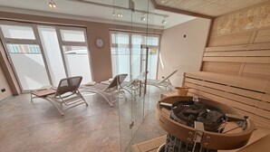 Ett modernt spa-rum med bastu, solstolar och en eldstad som är inramad av glas.
