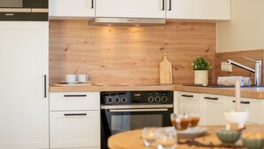 Ett modernt kök med vita skåp, en träpanel bakom arbetsbänken och en inbyggd ugn.