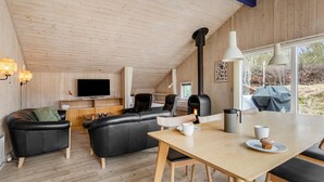 En mysig stuga med träpanel i taket, en soffa, ett matbord och en öppen spis.