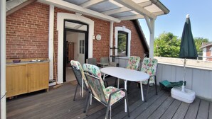 Eine überdachte Terrasse mit Backsteinmauer, Holzschrank, Tisch mit Stühlen und einem grünen Sonnenschirm.