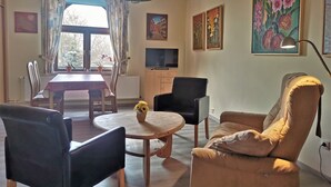 Ein Wohnzimmer mit Esstisch, Stühlen, einer Couch, einem Fernseher und Kunstwerken an den Wänden.