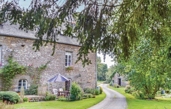 Un bâtiment en pierre doté d’une allée sinueuse, entouré d’une végétation luxuriante et agrémenté d’un petit patio avec des sièges d’extérieur.