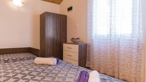 Un dormitorio con cama, armario, una mesita con un frutero y una ventana con cortinas estampadas.