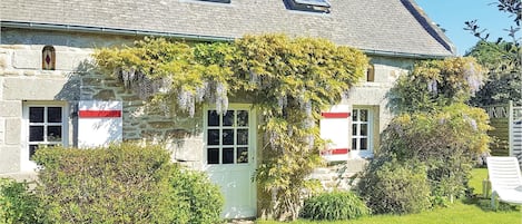 A stone house with a garden, a table with chairs, and a clear sky.