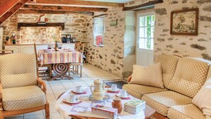 A cozy room with a dining table set for four, a sofa, and a kitchen area with stone walls. - 1 bedroom lovely home in Douarnenez (Douarnenez)