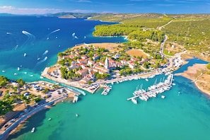 Luftaufnahme einer Küstenstadt mit einem Yachthafen, klarem türkisblauem Wasser und umgebender Vegetation.