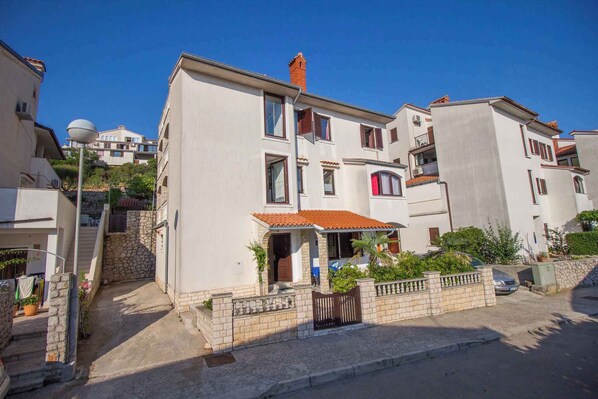 Un edificio residencial con escaleras de piedra, tejado de tejas rojas y un pequeño jardín.