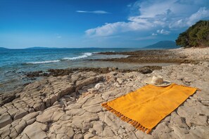 Una playa con una manta amarilla y un sombrero sobre las rocas.