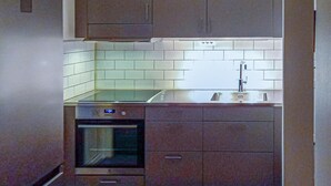 Une cuisine compacte dotée d’un four encastré, d’un évier en acier inoxydable et de carreaux de couleur claire.