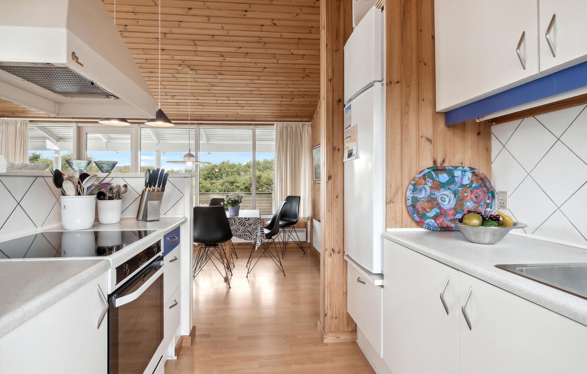 Una cocina moderna con armarios blancos, techo de madera y un comedor con mesa y sillas.
