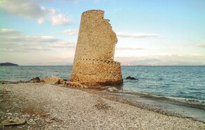 Eine Küstenstruktur aus Stein mit rauher, unebener Oberfläche, umgeben von einem Kiesstrand und ruhiger See.