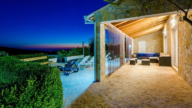 Un edificio revestido de piedra con un espacio al aire libre techado, que incluye sillones de lounge y un jacuzzi.