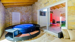 Una habitación de paredes de piedra con jacuzzi, una puerta y un ventanal que da a otra zona.