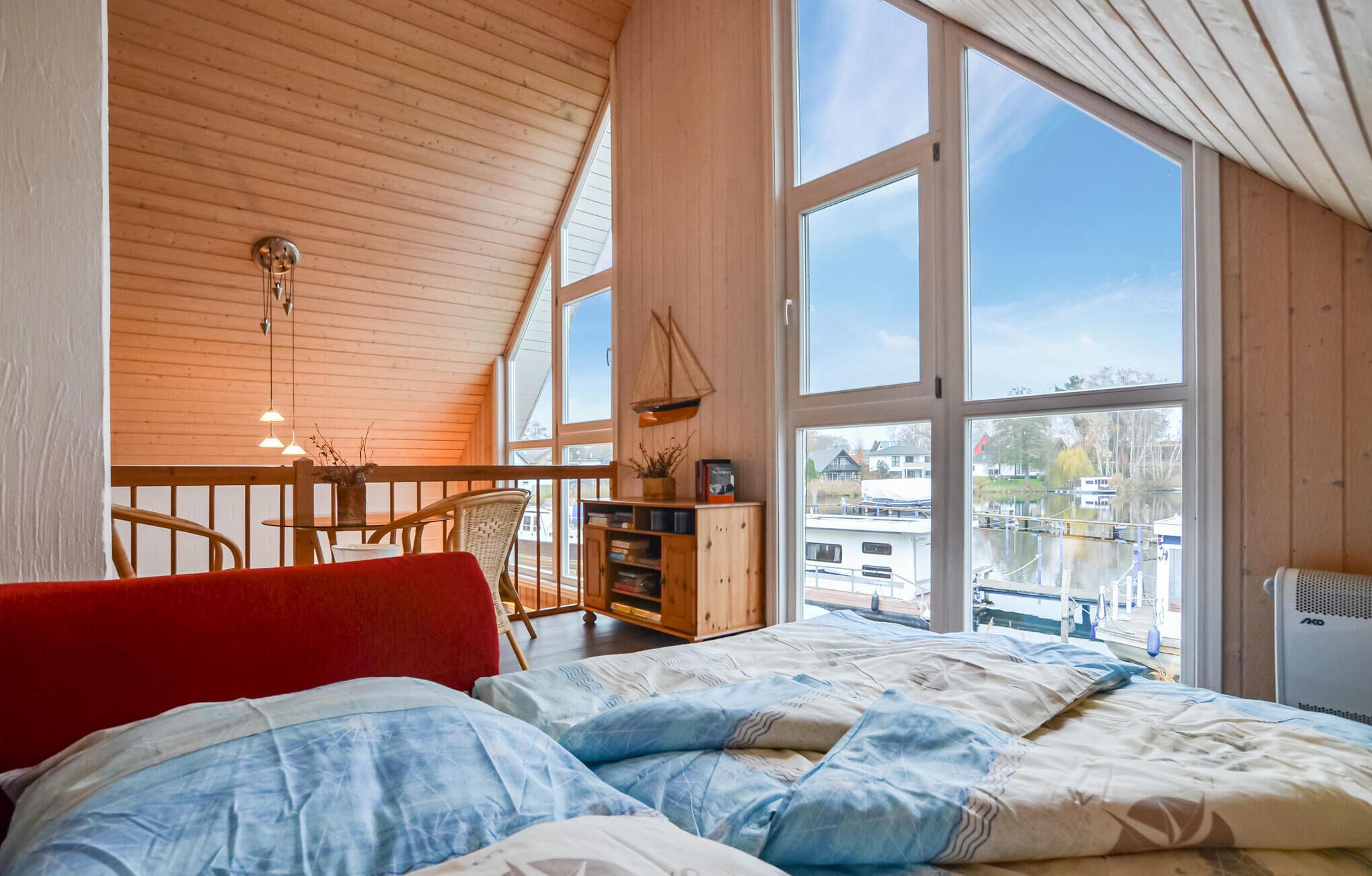 Une chambre confortable avec une grande fenêtre, un plafond en bois et une vue sur les bateaux à l’extérieur.
