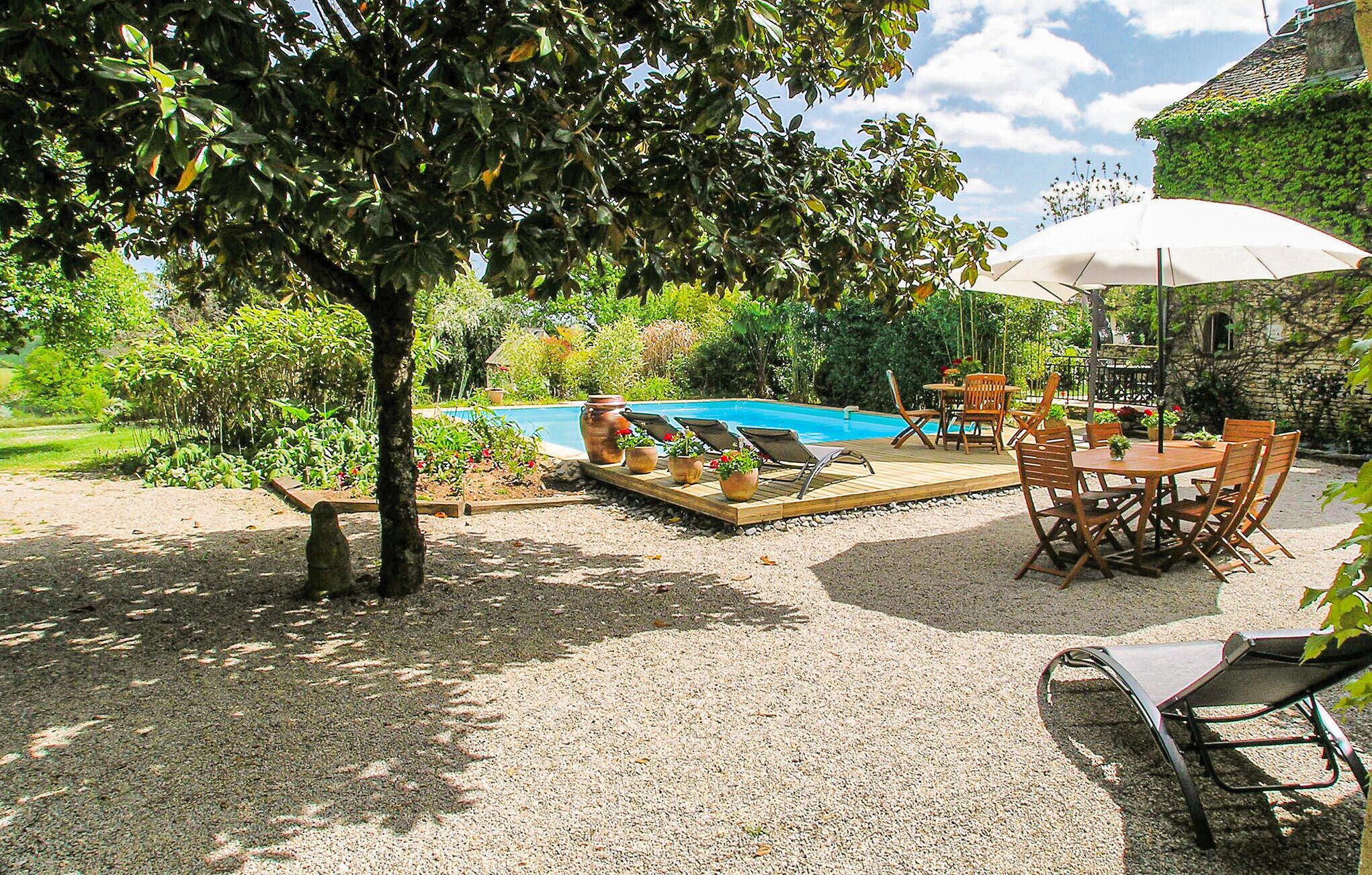 Un espace aménagé au bord de la piscine, avec une terrasse en bois, des chaises longues, une table avec des chaises et un parasol blanc.