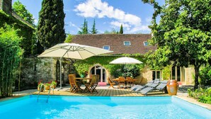 A swimming pool with lounge chairs and umbrellas, surrounded by greenery and a stone wall. - Amazing home in Les Farges (Les Farges)