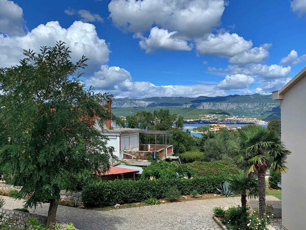 A residential area with a stone pathway, a tree, and a view of a town and mountains in the distance.