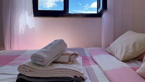 Una cama bien hecha con una colcha rosa y blanca a cuadros, una almohada blanca y una pila de toallas dobladas.