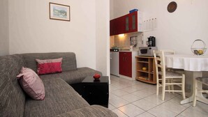 Un espacio habitable compacto con un sofá gris, una mesita auxiliar negra, una mesa de comedor con sillas y una zona de cocina con armarios rojos y un microondas.